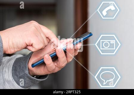Close-up of a caucasian unrecognizable person's hands holding and touching a mobile phone's screen and any icons are floating over the image. Stock Photo