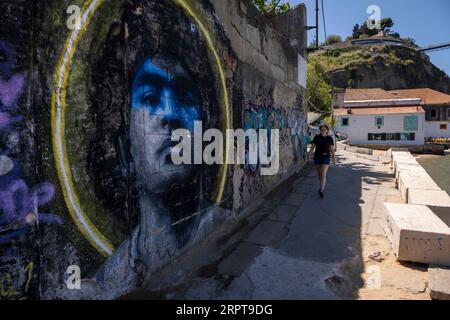 Almada, Portugal. 27th Aug, 2023. A woman seen walking near a wall with the image of soccer player Diego Maradona, in the town of Almada. Located on the south bank of the Tejo River, Almada is the best viewpoint over the city of Lisbon, with the castle, the panoramic elevator of Boca do Vento and the statue of Christ the King built in 1959, they are used as observation points. (Credit Image: © Jorge Castellanos/SOPA Images via ZUMA Press Wire) EDITORIAL USAGE ONLY! Not for Commercial USAGE! Stock Photo