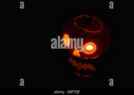 Close-up on a Jack O' Lantern lit in the dark and reflecting on a black surface in front of it. Stock Photo