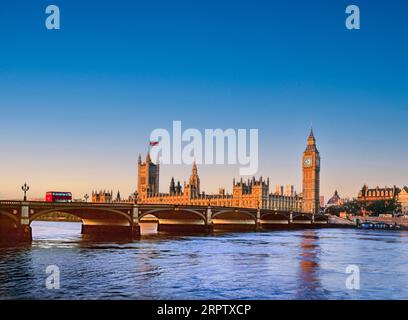 Houses of Parliament Westminster UK flying the Union Jack flag illuminated by dawn first light sunrise, red London bus on Westminster Bridge. River Thames at high tide from South Bank London UK. London scenic view landscape travel destination Stock Photo