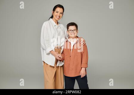 middle aged woman and son with down syndrome wearing stylish clothes and holding hands on grey Stock Photo