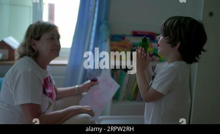 Child interacting with grandmother in bedroom. Candid authentic grandma's relationship with her grandson Stock Photo