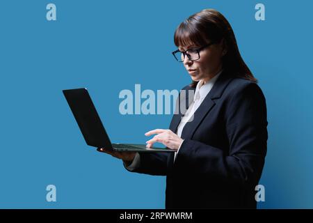 Serious mature woman using laptop, on blue background Stock Photo