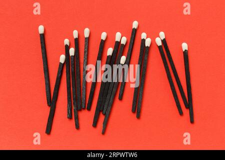 Black matches with white sulfur heads, isolated on red background, top view. Black and white matches, smoking accessories. Stock Photo