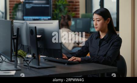 Asian software developer focused on writing code encounters unexpected compiling error sitting at desk in cyber security development office. Programer having system failure while creating algorithm. Stock Photo
