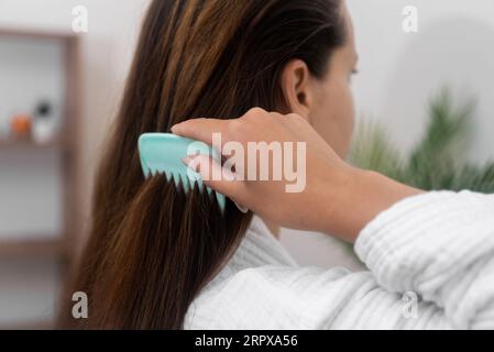 Woman combing long healthy chestnut hair in bathroom closeup lady in bathrobe taking care of hair Stock Photo