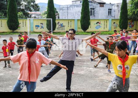 200620 -- WUXUAN, June 20, 2020 -- Wei Xuxi takes exercise with students during a break at Shuanggui Primary School in Ertang Town of Wuxuan County, south China s Guangxi Zhuang Autonomous Region, June 19, 2020. Wei Xuxi, a 57-year-old teacher of Ertang Town in Wuxuan County, has spent over 30 years teaching in the countryside after graduating from high school in 1985. There are 32 students in two grades in Shuanggui Primary School, a small-scale school where Wei works. Instead of dilapidated buildings, or broken tables and chairs, multimedia and many other advanced teaching equipment make the Stock Photo