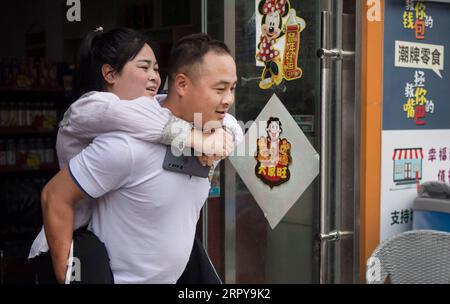 200621 -- ANKANG, June 21, 2020 -- Li Peng, carrying his sister Li Dan on his back, walks out of a store in a market in Ankang City, northwest China s Shaanxi Province, June 19, 2020. In 1997, in order to shake off poverty, Li Zengyi, a villager in Wenhua Village of Ankang City, moved his family, including his seven-year-old disabled daughter, to a makeshift house on a mountain to cultivate peaches. Li Wei, the elder son of Li Zengyi, went out to work in south China s Guangdong Province after graduation from middle school to support the family. Li Peng, the younger son, continued his study unt Stock Photo