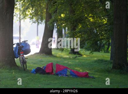 Hamburg, Germany. 05th Sep, 2023. A homeless man lies in his sleeping bag next to his bicycle on a meadow at the Kennedy Bridge. On Thursday, the groundbreaking ceremony for the new building for the 'Pik As' overnight shelter for homeless men is to take place. Credit: Marcus Brandt/dpa/Alamy Live News Stock Photo