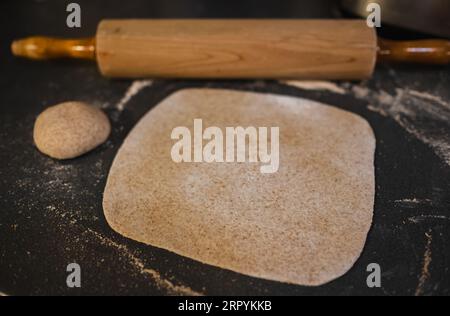 Rolled out wholemeal dough, wheat, grain with vintage rolling pin on the table. Homemade organic dough. Rolled dough on the table. Stock Photo