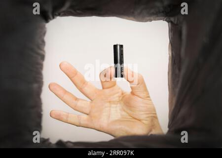 Disposal of batteries. A man puts old used AA batteries in a trash can. Bottom view. Stock Photo