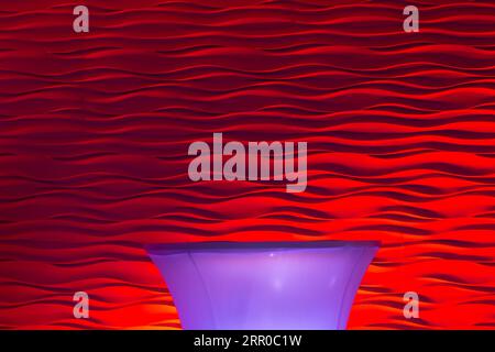 A wall draped with a red pleated fabric, illuminated by a beautiful light. A table covered with purple fabric against the background of the wall. Stock Photo