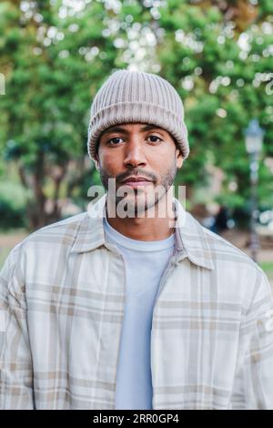 Vertical close up individual portrait of young attractive african american man with beanie hat looking serious at camera. Front view of a hispanic guy standing in a park outdoors with sad attitude. High quality photo Stock Photo