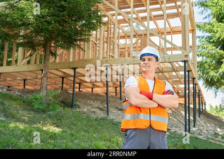 Young man, builder wearing uniform and helmet, standing with crossed hands, admiring forest. Stock Photo