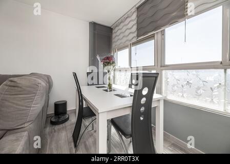 White wooden dining table with black chairs next to a large window with city views Stock Photo