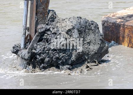 Dredging the bottom of water area, view of the bucket of the floating excavator full of mud Stock Photo