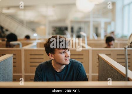 Smiling young man looking away while sitting in library at university Stock Photo