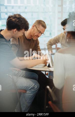 Mature professor assisting students in classroom at university Stock Photo