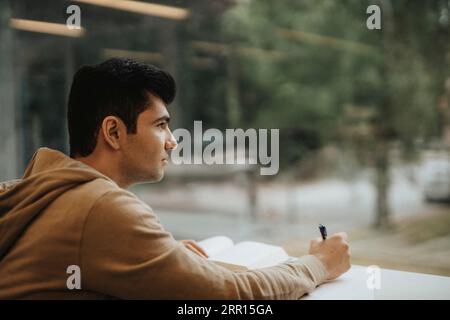 Thoughtful young male student studying at table in university Stock Photo