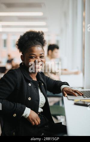 Portrait of smiling female student sitting with laptop at table in university Stock Photo