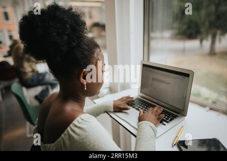 Side view of female student using laptop at table in university Stock Photo
