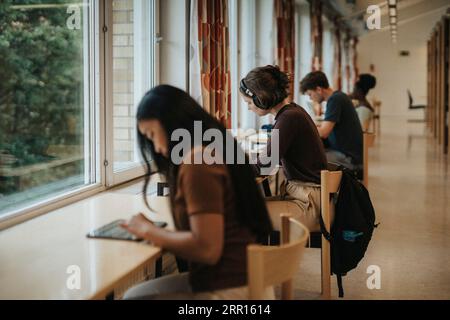 Side view of young woman wearing headphones studying in library at university Stock Photo