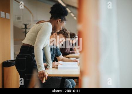 Happy multiracial male and female students discussing over book in library Stock Photo
