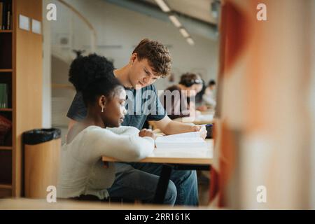 Multiracial male and female students discussing over book in library at university Stock Photo