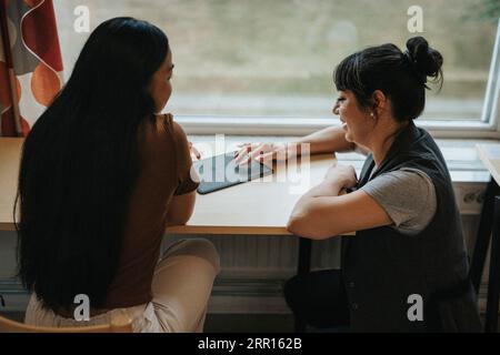 Side view of happy professor discussing over tablet PC at table in library Stock Photo
