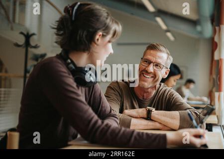 Happy professor discussing with student in library at university Stock Photo