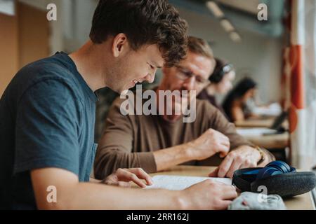 Smiling male student studying under guidance of professor in library Stock Photo
