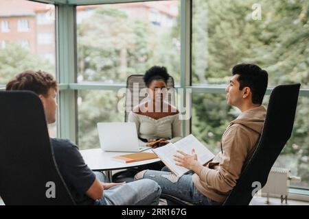 Multiracial students discussing while studying together in university Stock Photo
