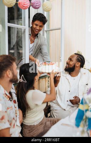 Smiling young man giving cake to male and female friends sitting at cafe Stock Photo