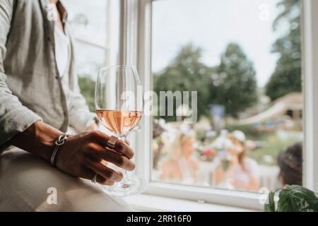 Midsection of young man holding wineglass sitting near window in cafe Stock Photo