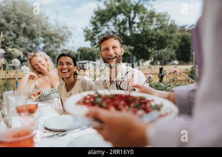 Happy male and female friends laughing while sitting at table during dinner party Stock Photo