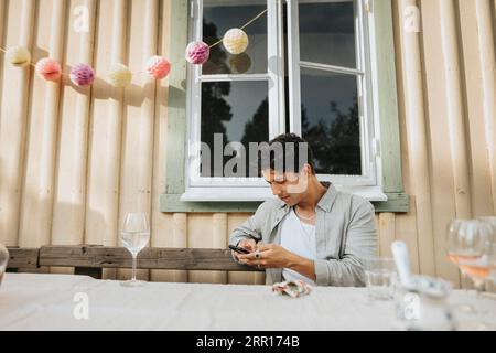 Young man using smart phone while sitting at table during dinner party Stock Photo