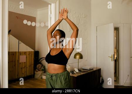 Young woman exercising with eyes closed and arms raised at home Stock Photo