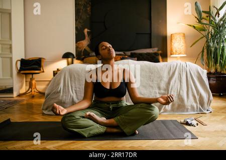 Young woman meditating on exercise mat in bedroom at home Stock Photo
