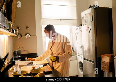 Young woman holding grapes using laptop in kitchen at home Stock Photo