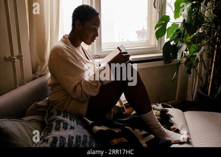 Side view of young woman writing in book while sitting on bed at home Stock Photo