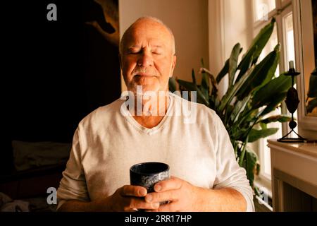 Senior man with eyes closed holding coffee cup at home Stock Photo