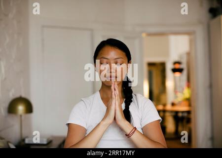 Young woman with hands clasped meditating at home Stock Photo