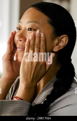 Young woman applying moisturizer on face at home Stock Photo