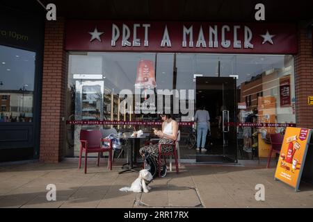 Young woman sat with her dog outside a Pret A Manger branch surfing on her smartphone in Wimbledon, Southwest London, England, United Kingdom Stock Photo