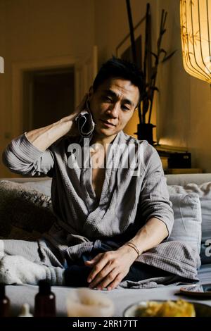Man wiping sweat while sitting on sofa at home Stock Photo