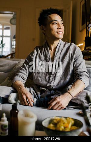 Smiling man looking away while sitting on sofa at home Stock Photo