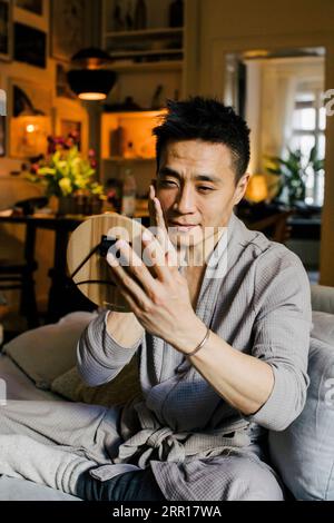 Man looking in mirror while sitting on sofa at home Stock Photo