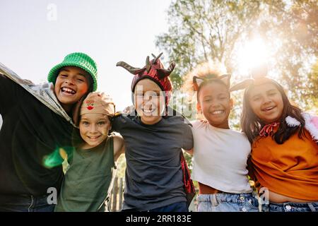 Low angle portrait of happy kids wearing headbands standing with arms around at summer camp Stock Photo