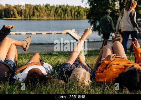 Boy pointing while lying down with friends on grass at summer camp Stock Photo