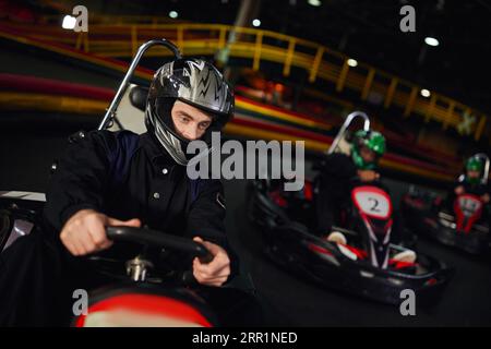 concentrated diverse men in helmets driving go kart on indoor circuit, motorsport and adrenaline Stock Photo